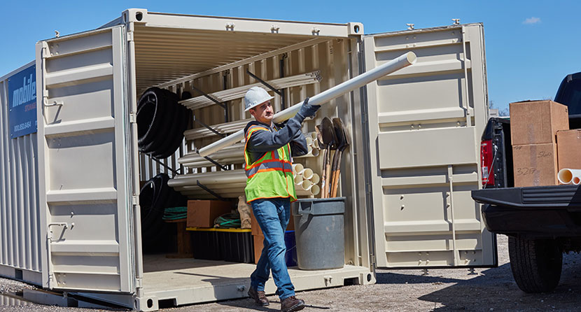 Worker carrying materials out of a WillScot storage container on a job site.
