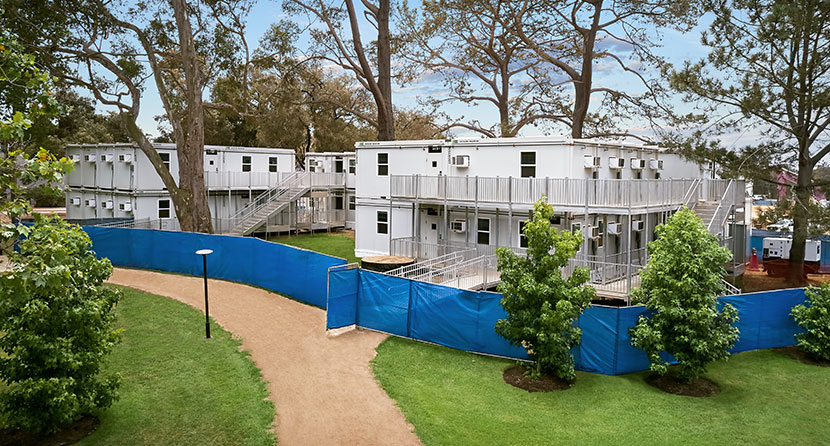 A photograph of 2-story stacked white FLEX mobile offices, situated among surrounding trees