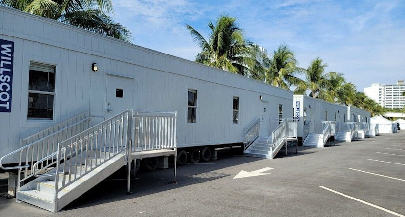 Photograph of several WillScot mobile trailer offices lined up in a parking lot on a bright summer day with palm trees in the background.